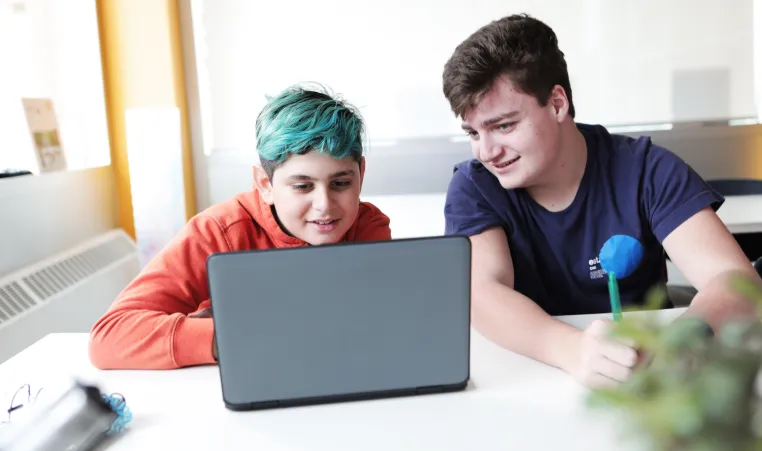 Two teenage boys watch something on a laptop.