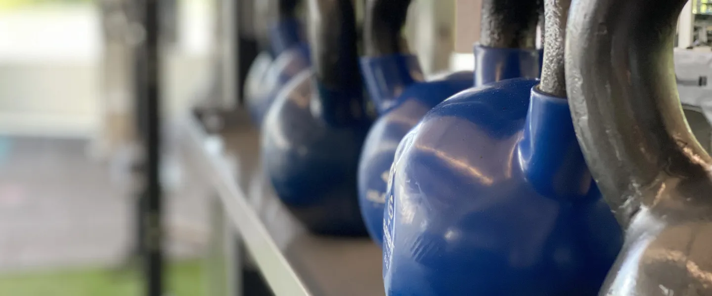 A row of blue and grey kettlebells sits in the turf fitness zone area of a YMCA.