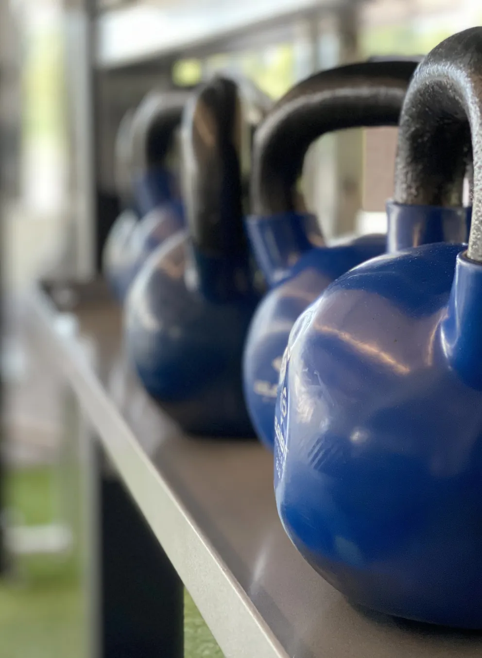 A row of blue and grey kettlebells sits in the turf fitness zone area of a YMCA.