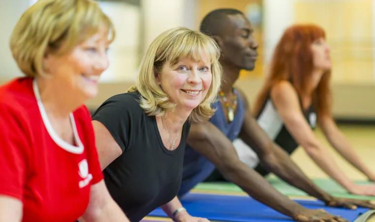Two older blonde women participate in a group yoga class.