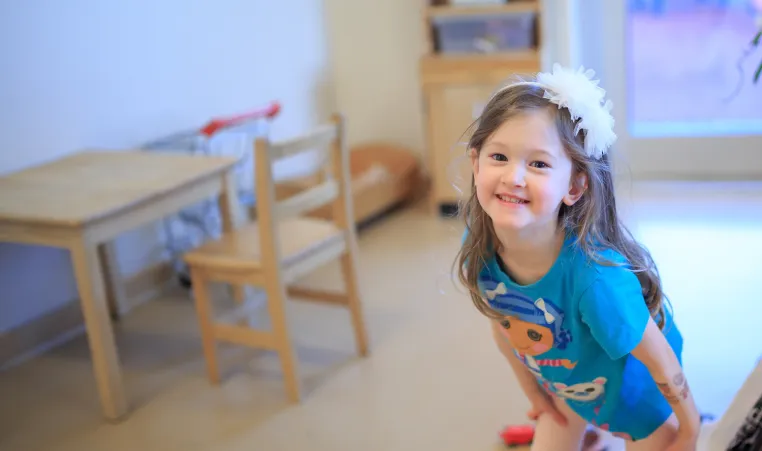 A young girl in a blue tshirt and white flower headband smiles for the camera at a YMCA Child Care Centre.