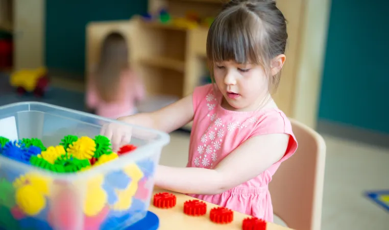 A young girl wearing a pink flower shirt plays with building toys at a table in a YMCA child care centre.