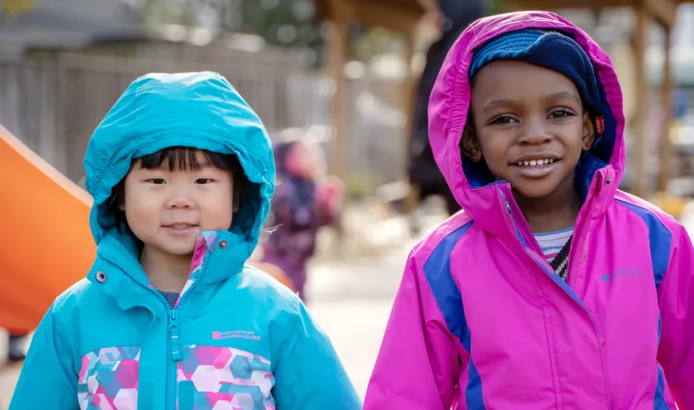 Two girls in bright spring coats, stay bundled while playing outside.