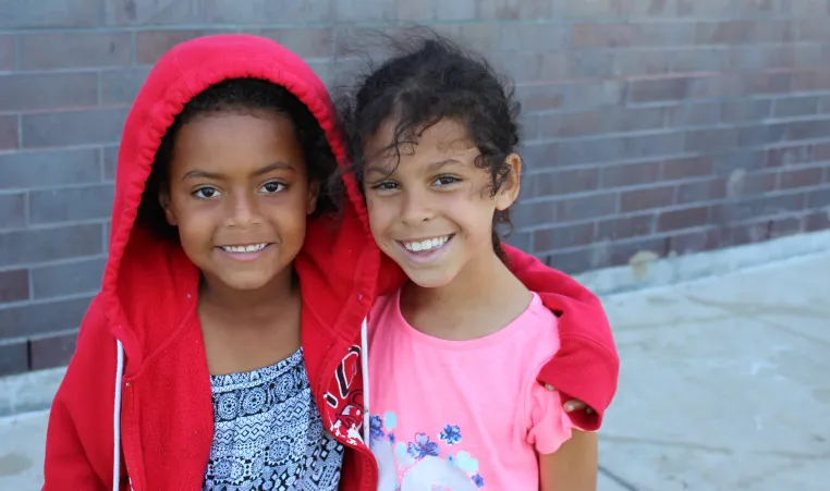 A girl in a red hoodie puts her arm around her friend in a pink t-shirt at YMCA Day Camp.