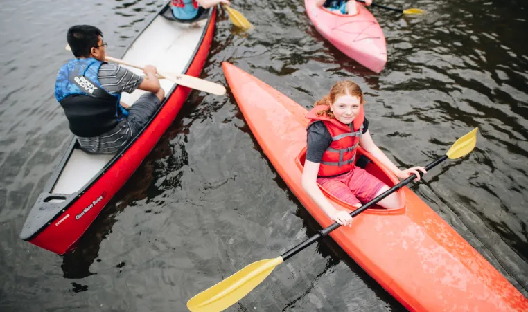 A group of kids paddle on the lake in canoes and kayaks.