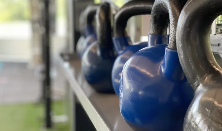 A row of blue and grey kettlebells sits in the turf fitness zone area of a YMCA.