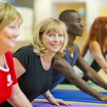Two older blonde women participate in a group yoga class.