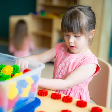 A young girl wearing a pink flower shirt plays with building toys at a table in a YMCA child care centre.