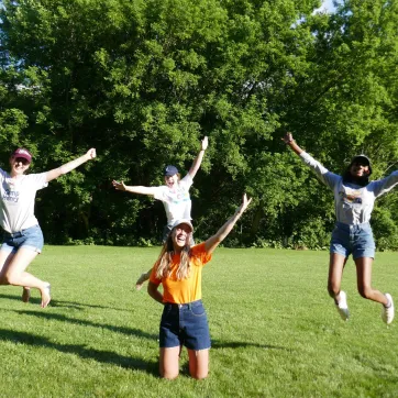 The YMCA Overnight Camp team jump and smile in a grassy field.