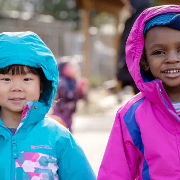 Two girls in bright spring coats, stay bundled while playing outside.