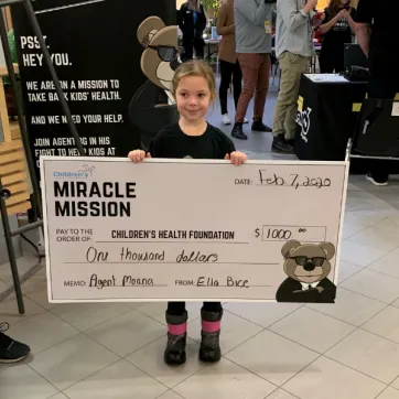 Ella holds a cheque for $1000 dollars she helped raise for the Children's Hospital.