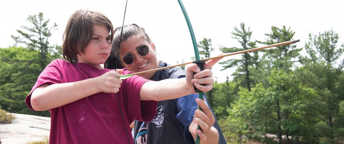 CQE counselor teaching a camper about how to shoot an arrow during archery hour