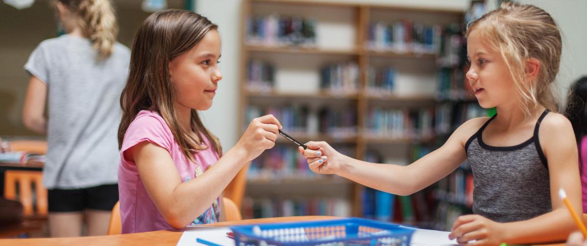 Two girls colouring and sharing a pencil crayon